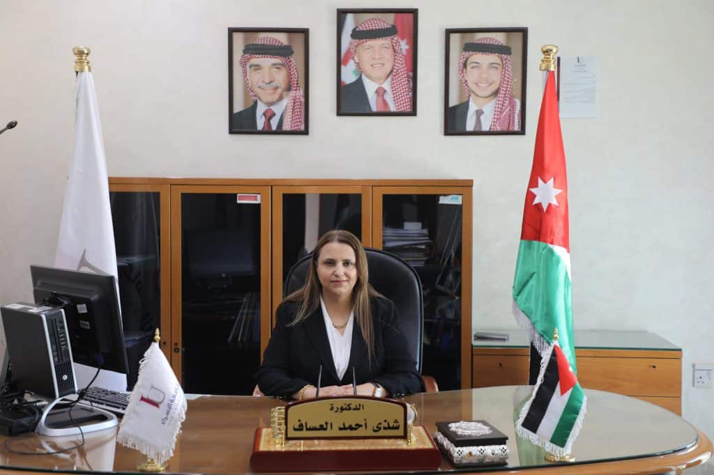 صورة لمديرة تجلس خلف مكتبها في جامعة الأردنية، مع صور لملوك الأردن على الحائط وعلم الأردن بجانبها.
